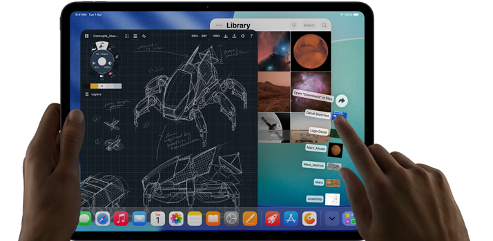 iPad Pro, space black color, left hand holding device, right hand pointing gesturing to manipulate multiple open app windows, a drawing app with sketches of mechanical designs, photos library of planets and space images, downloads folder files fanned out
